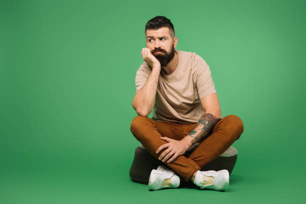 Bored handsome bearded man sitting on green