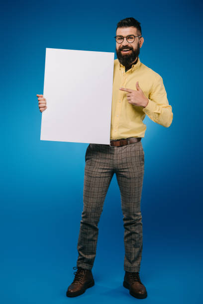 istock bearded smiling man pointing at empty placard isolated on blue 1144520363