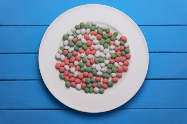 istock White plate with color preparations (vitamins, dyes, flavor enhancers, nutritional supplements, innovative technologies, candy sweets) on an blue wooden table background. 1144520541