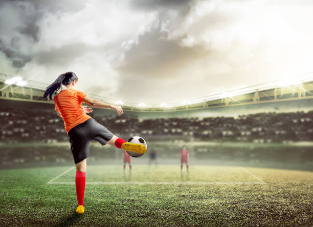 vista trasera de la mujer del jugador de fútbol asiático en jersey de color naranja golpeando la pelota - back and forwards fotografías e imágenes de stock
