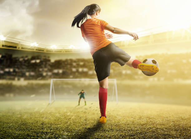 Rear view of asian football player woman in orange jersey kicking the ball in the penalty box Rear view of asian football player woman in orange jersey kicking the ball in the penalty box on football field at stadium scoring a goal photos stock pictures, royalty-free photos & images