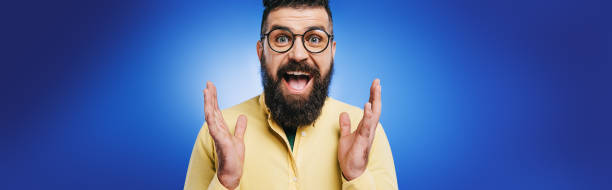 istock excited handsome man in eyeglasses gesturing isolated on blue 1144520995
