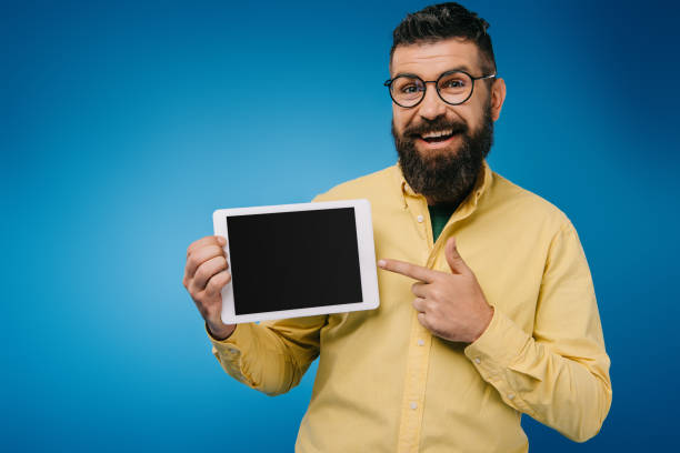 istock handsome smiling man pointing at digital tablet with blank screen, isolated on blue 1144521167