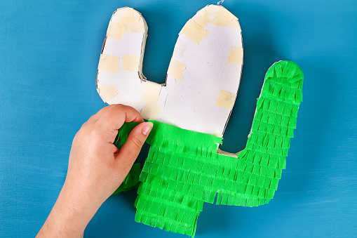 Diy cinco de mayo Mexican Pinata Cactus made cardboard and crepe paper your own hands on a blue background. Gift idea, decor, game cinco de mayo. Step by step. Top view. Process kid children craft.