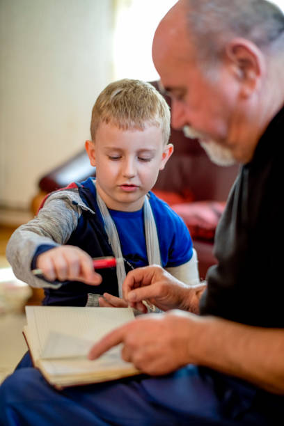 istock Little boy with broken arm doing homework with his grandfather 1144523436