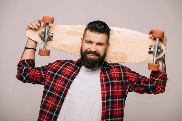 istock smiling bearded man in checkered shirt posing with longboard isolated on grey 1144525436
