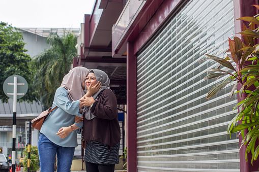 Happy together - muslim adult daughter hugging and kissing mother outdoor on city sidewalk
