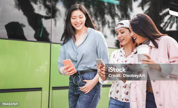 Happy Asian Friends Using Smartphones At Bus Station Young Students People Having Fun With Technology Trends After School Friendship And Transports App Concept Focus On Center Girl Face Stock Photo - Download Image Now