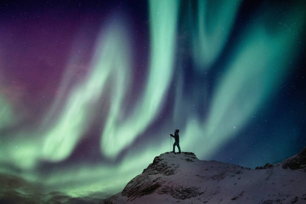 istock Man climber standing on snowy peak with aurora borealis and starry 1144527680