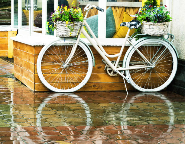 White vintage bicycle with floral baskets White vintage bicycle with floral baskets standing outside at cafe background. Retro style transport with beautiful flowers rainy cafe stock pictures, royalty-free photos & images