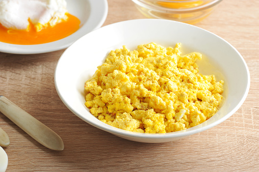 Scrambled eggs from chicken eggs in a white deep plate. Close-up. Light wooden background.