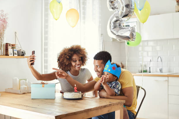 Family taking selfie while celebrating birthday Smiling woman taking selfie with man and boy at table. Parents are sitting with son in kitchen. Family is making memories while celebrating birthday at home. number 2 photos stock pictures, royalty-free photos & images