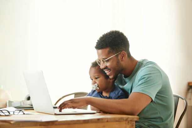 istock Smiling father holding son while working on laptop 1144539411