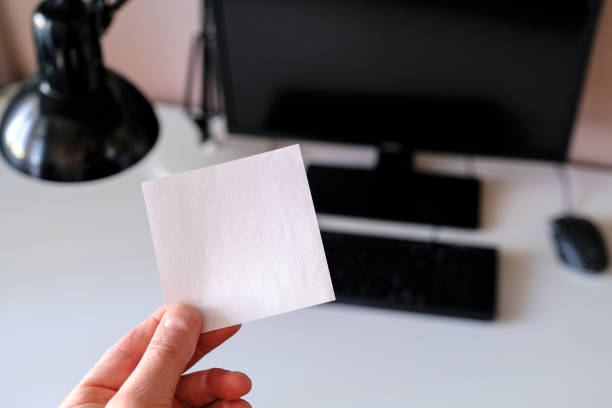 istock Sticker in hand, on desktop background with computer and keyboard in the background. 1144540176