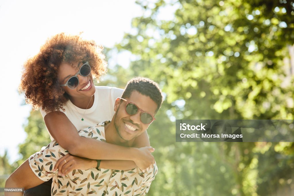 Young couple enjoying piggyback ride on sunny day Young couple enjoying piggyback ride on sunny day. Smiling man and woman are spending leisure time in city. They are on vacation. Couple - Relationship Stock Photo