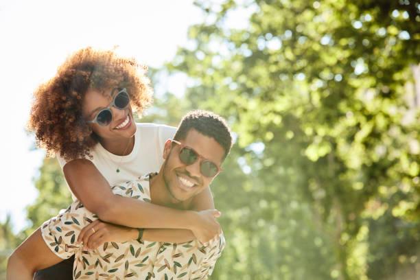 Young couple enjoying piggyback ride on sunny day Young couple enjoying piggyback ride on sunny day. Smiling man and woman are spending leisure time in city. They are on vacation. african american couple stock pictures, royalty-free photos & images