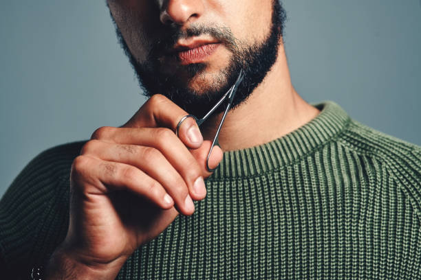 How he keeps his beard looking good Cropped studio shot of a young man trimming his beard against a grey background beard stock pictures, royalty-free photos & images