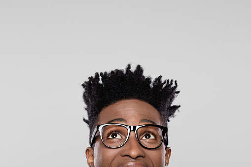 Close up of afro american man with eyeglasses looking upwards with surprised expression. Half face of young guy with funky hairstyle wearing nerdy glasses and looking at copy space.