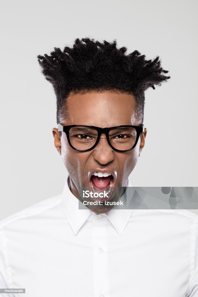 Afro american businessman looking furious Portrait of afro american businessman looking furious. Man in white shirt wearing eyeglasses with funky hairstyle on gray background. African Ethnicity Stock Photo