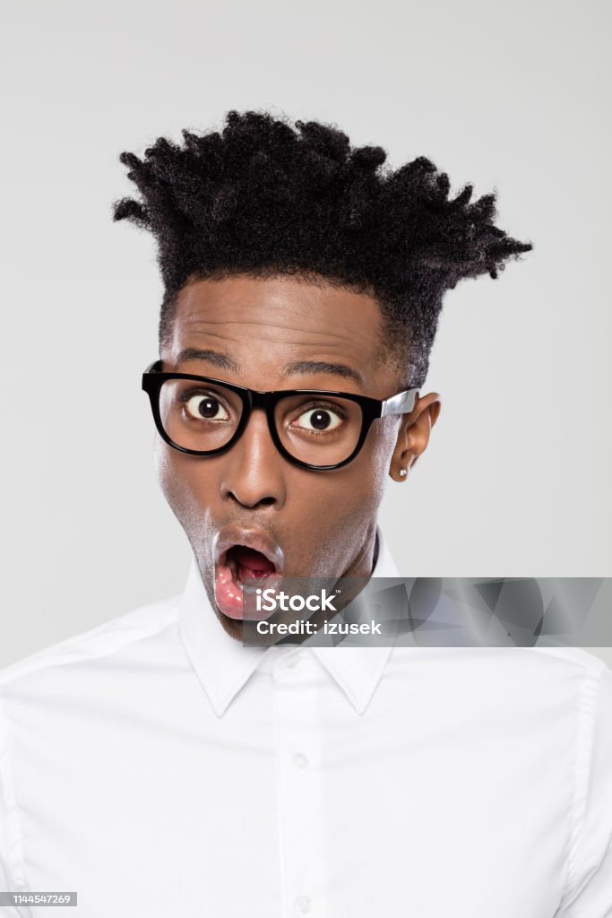 Funky businessman looking surprised Close up portrait of surprised young african man wearing nerd glasses against gray background. Funky businessman with mouth open. Adult Stock Photo