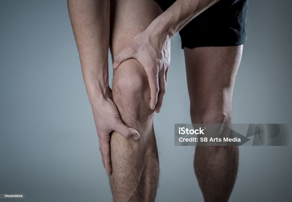Young fit man holding knee with hands in pain after suffering muscle injury broken bone leg pain sprain or cramp during running workout. In Body pain and sport training injury and body health care. Knee Stock Photo