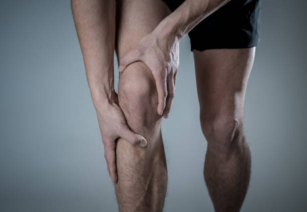 Young fit man holding knee with hands in pain after suffering muscle injury broken bone leg pain sprain or cramp during running workout. In Body pain and sport training injury and body health care. stock photo