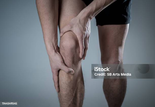 Young Fit Man Holding Knee With Hands In Pain After Suffering Muscle Injury Broken Bone Leg Pain Sprain Or Cramp During Running Workout In Body Pain And Sport Training Injury And Body Health Care Stock Photo - Download Image Now