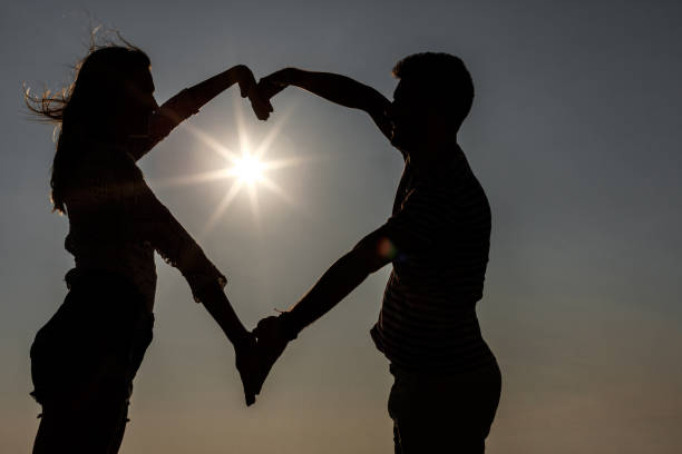 Couple making heart shape with arms during sunset