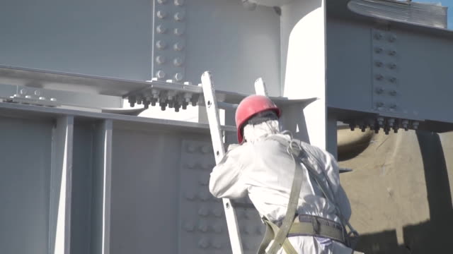 The worker in a protective suit paints with white paint building constructions.