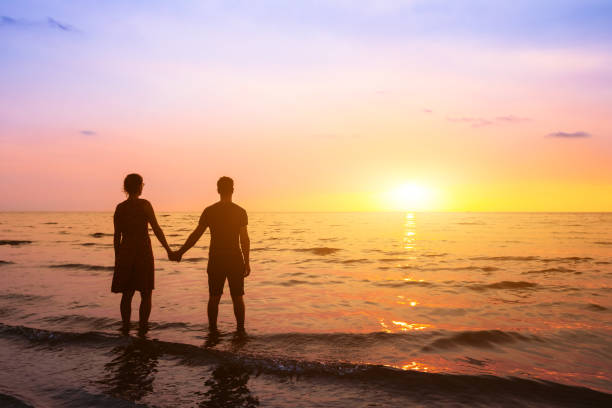 romantyczna para na plaży o zachodzie słońca obserwując horyzont, wakacje na miesiąc miodowy w miejscu morza, sylwetka dwóch kochanków trzymających się za rękę - romance tropical climate ideas travel destinations zdjęcia i obrazy z banku zdjęć