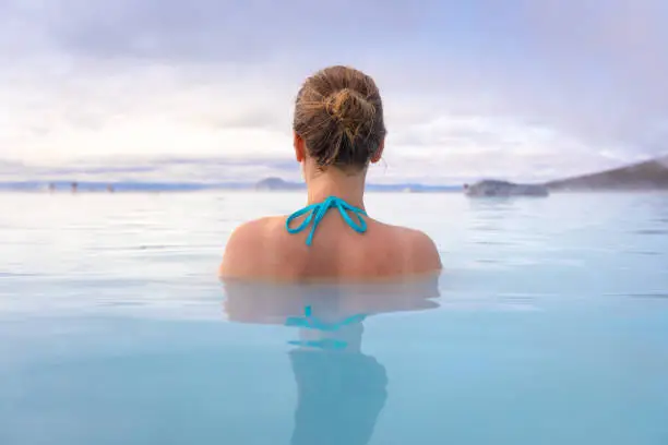 Geothermal spa in Iceland with young woman enjoying bathing in hot thermal pool with hotspring water for wellness and skin treatment, Icelandic experience