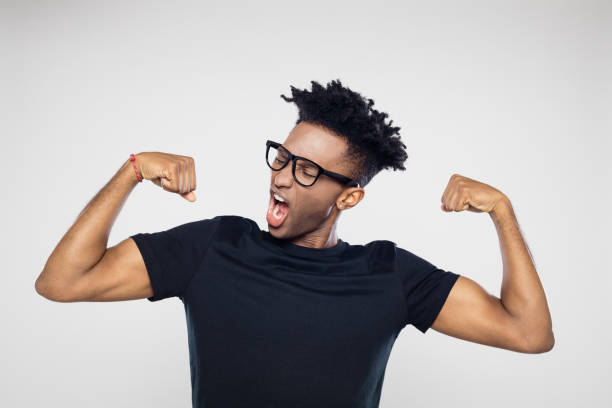 Afro american man flexing arms Portrait of excited young afro american man flexing his arms against gray background black nerd stock pictures, royalty-free photos & images