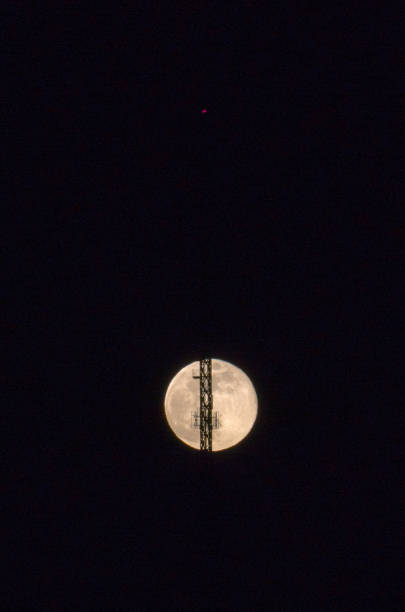 full moon rising into the night sky with a radio antenna and transmission tower with a red signal light - full moon audio imagens e fotografias de stock