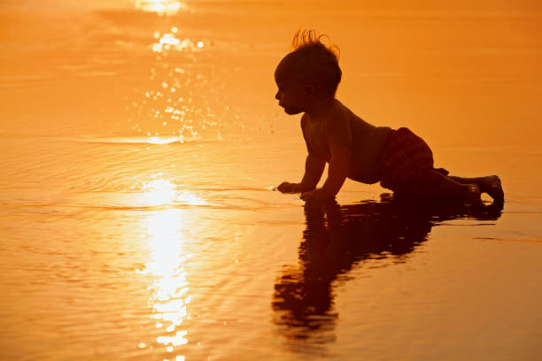 Little boy playing with squirt gun standing on the beach in the sea.