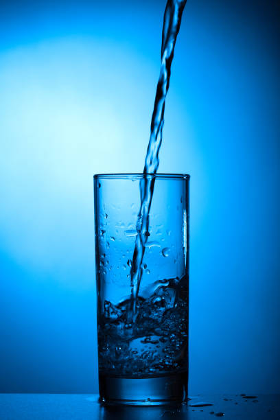 istock Pouring water into glass on blue background 1144558795