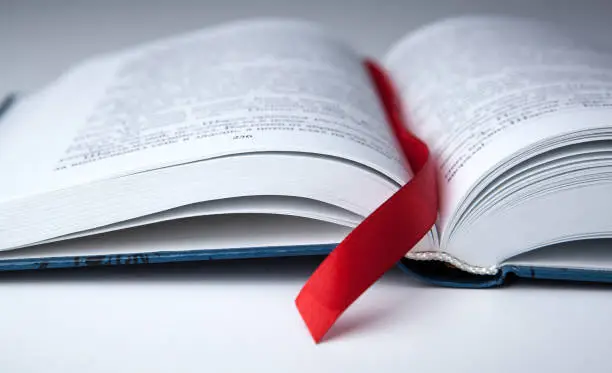 Photo of new open book on a gray table with a red ribbon bookmark close up