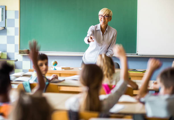 istock Happy mature elementary teacher aiming at school kids to answer her question. 1144563153