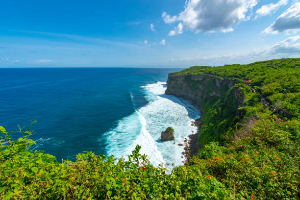 People walking along a path at the coastline of the tropical island of Bali, Indonesia, seen during a hot day in the summer.