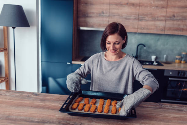 Woman holding baking tray with backed chicken nuggets Woman holding hot baking tray with backed chicken nuggets fish stick stock pictures, royalty-free photos & images