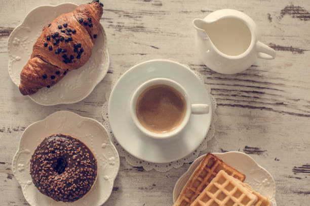 Donut, waffles, croissants and coffee on the wooden table, directly above.