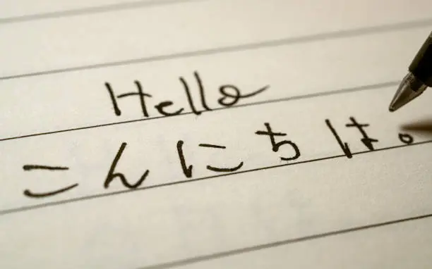 Photo of Beginner Japanese language learner writing Hello word in Japanese hiragana characters on a notebook close-up shot