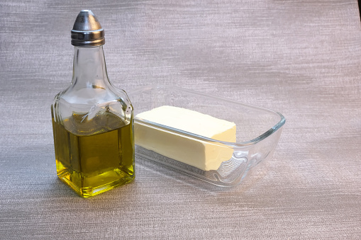 A small bottle of olive oil and glassware with butter on the table with a gray tablecloth