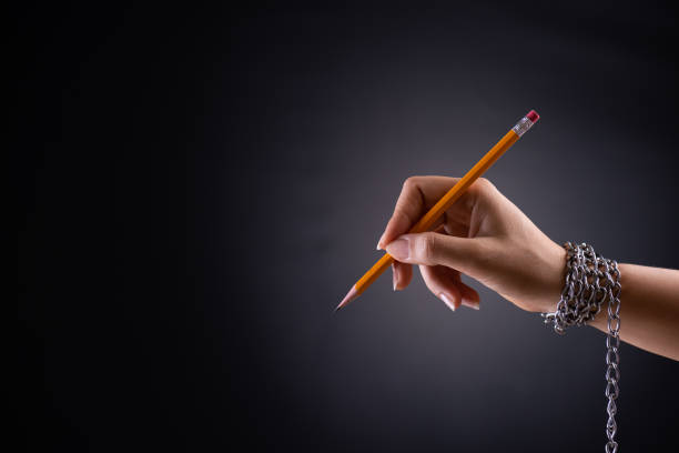 mano donna con matita gialla legata a catena, raffigurante l'idea di libertà di stampa o libertà di espressione su sfondo scuro in low key. libertà di stampa mondiale e concetto di giornata internazionale dei diritti umani. - cable stayed foto e immagini stock