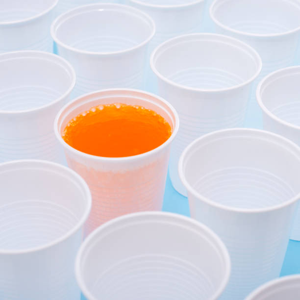 istock Disposable plastic white empty cups and one glass filled with orange lemonade 1144575253