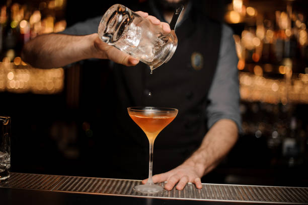 istock Bartender pouring an alcoholic drink from the measuring cup through the strainer to the cocktail glass 1144575805