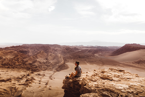 Silhouette of young woman staying at the edge of the cliff and looking at desert landscape during sunset in Atacama region, Chile