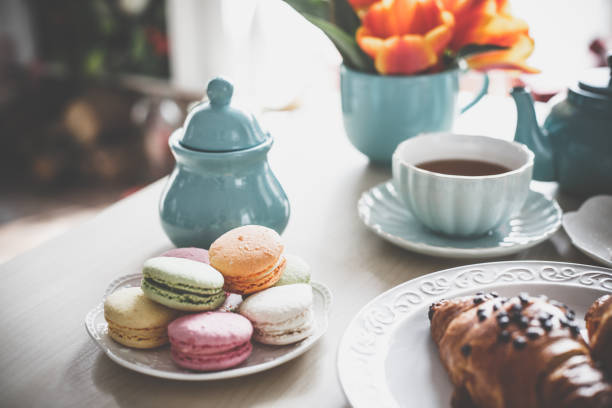 Tea cup, tea pot, macaroons, croissants and tulips on the coffee table.