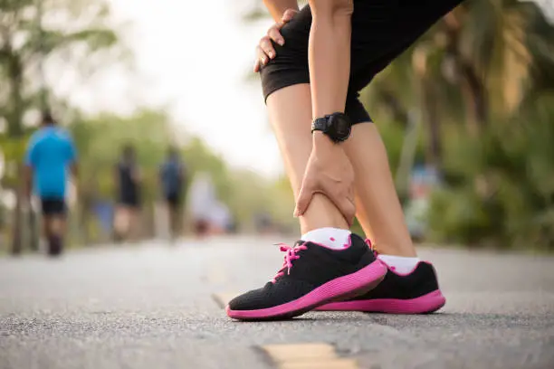 Photo of Woman suffering from an ankle injury while exercising. Running sport injury concept.