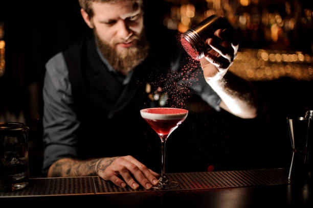 istock Professional bartender with a beard adding to a cocktail with a whipped cream a red powder 1144579497