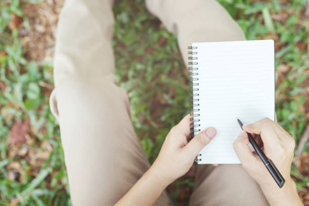 istock close up hand young man are sitting using pen writing Record Lecture notepad into the book in the parks.	top view Leave copy space empty to write messages. 1144581012